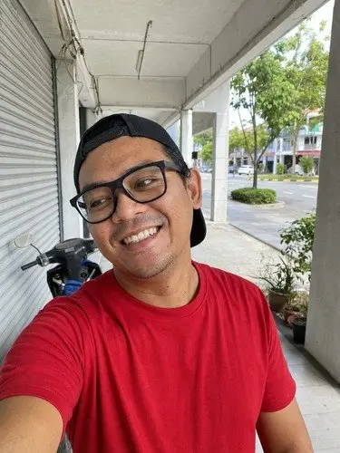 Selfie seorang lelaki bercermin mata, topi terbalik dan baju merah, sebelum diubah. Contoh dijana AI.